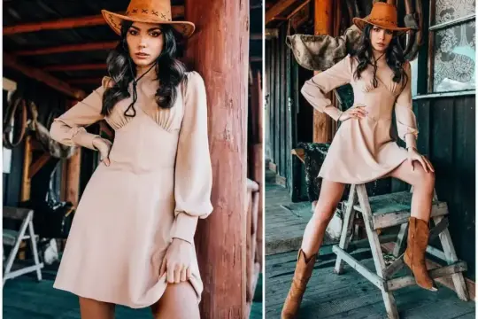 Dziewczyna w kapeluszu kowbojskim i beżowej sukience, z czarną bandaną przy spodniach, pozuje na tle drewnianej chaty.
